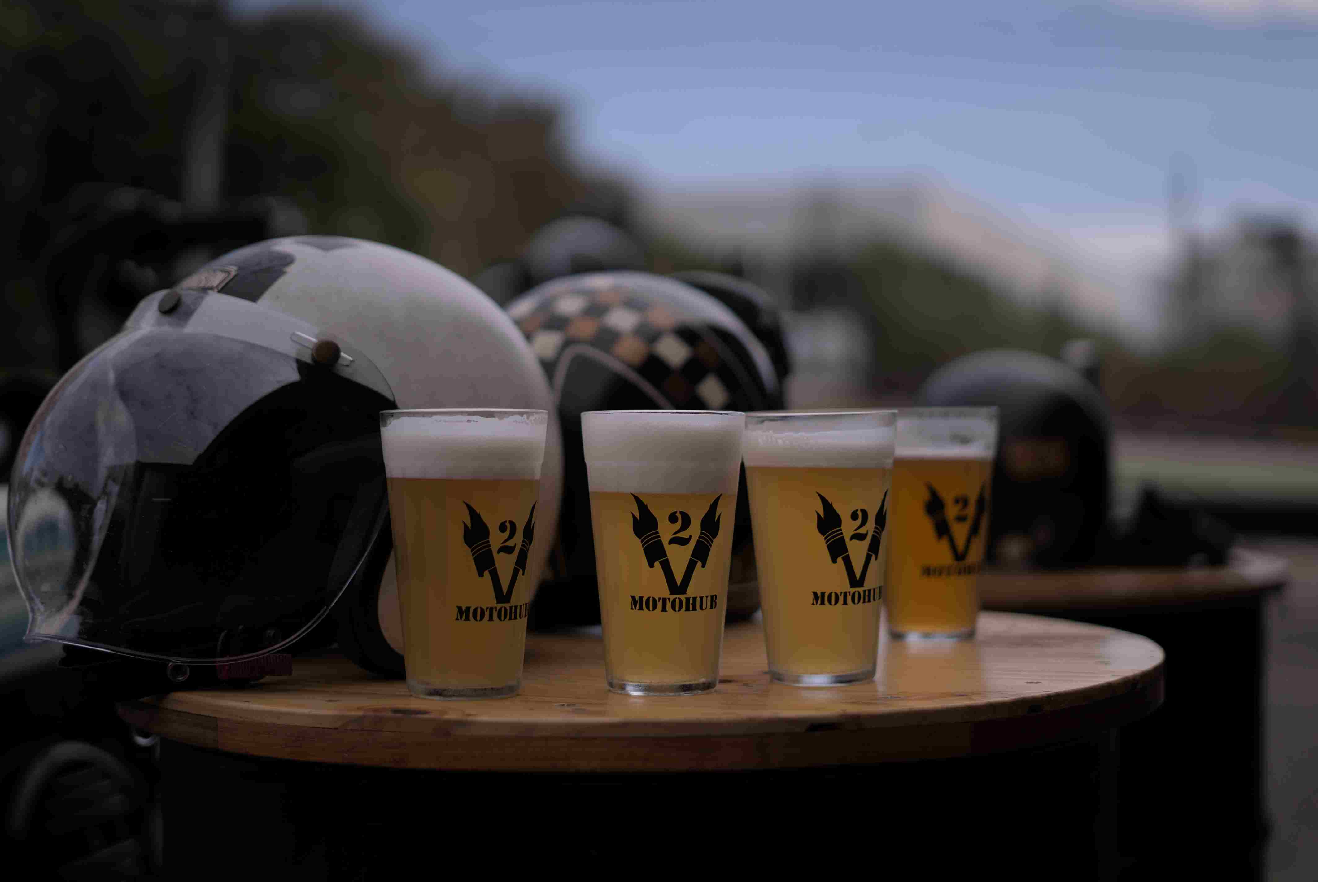 Cervejas V2 com capacetes e motos ao fundo